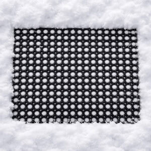 Black rubber ring mat lying in snow, with snow filling the open holes.