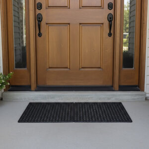 Two interlocking black rubber mats connected side by side in front of a wood double front door.