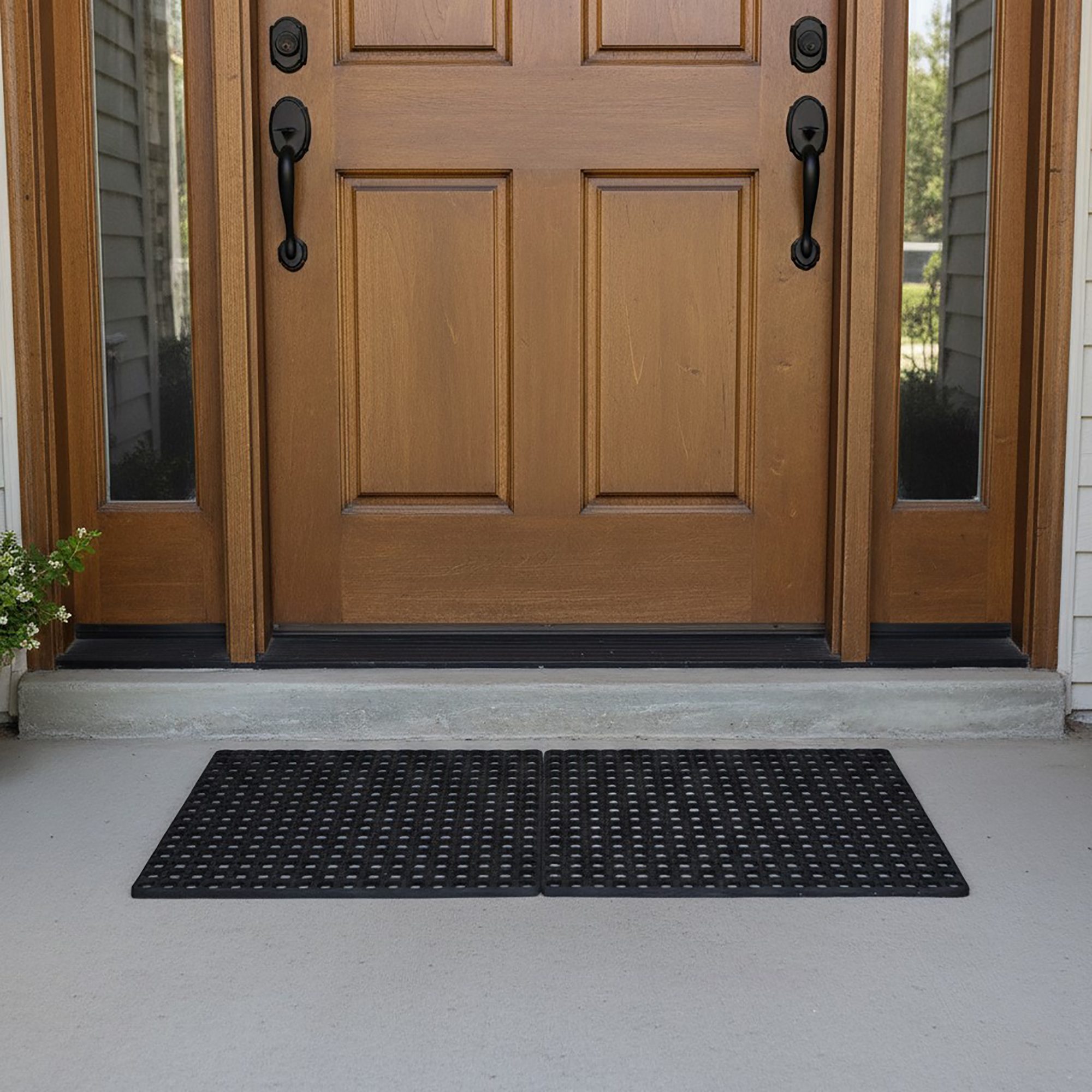 Two interlocking black rubber mats connected side by side in front of a wood double front door.