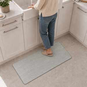 7- Person standing on gray anti-fatigue kitchen mat at the sink, cushioned comfort underfoot while washing up.