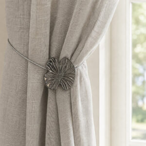 Lifestyle grège: Polished graphite water lily magnetic tieback holding a light gray sheer linen curtain by a sunlit window