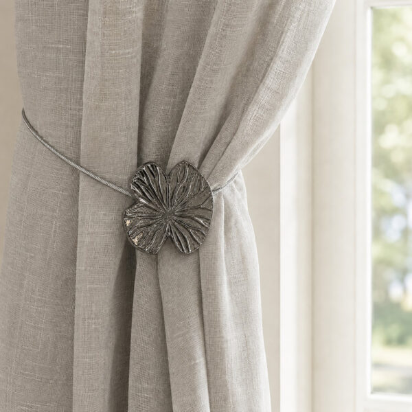 Lifestyle grège: Polished graphite water lily magnetic tieback holding a light gray sheer linen curtain by a sunlit window