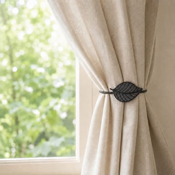 Gray leaf tieback holding a linen curtain back beside a sunny window
