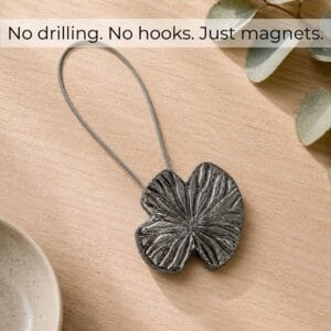 Flat-lay bois: Polished graphite water lily magnetic curtain tieback on light wood with eucalyptus, no drilling no hooks just magnets
