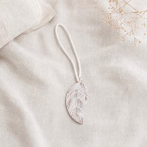 Single white leaf magnetic curtain tieback resting on natural linen fabric