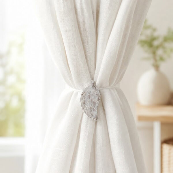 White leaf magnetic tieback holding back a light linen curtain by a bright window