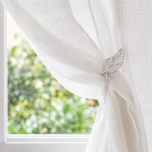 White leaf magnetic tieback holding a sheer voile curtain in a sunlit room