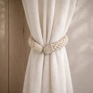 "Ecru rope tieback wrapped around a gathered sheer curtain against a wood-toned wall"