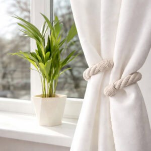 "Ecru cotton rope tieback on white curtain beside a potted plant on a windowsill"