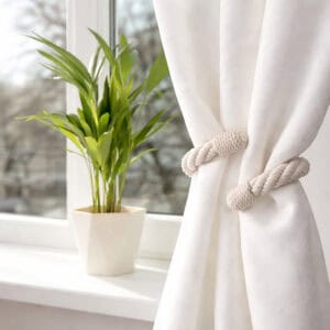 "Ecru cotton rope tieback on white curtain beside a potted plant on a windowsill"