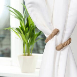 "Jute rope tieback on white curtain beside a potted plant on a windowsill"