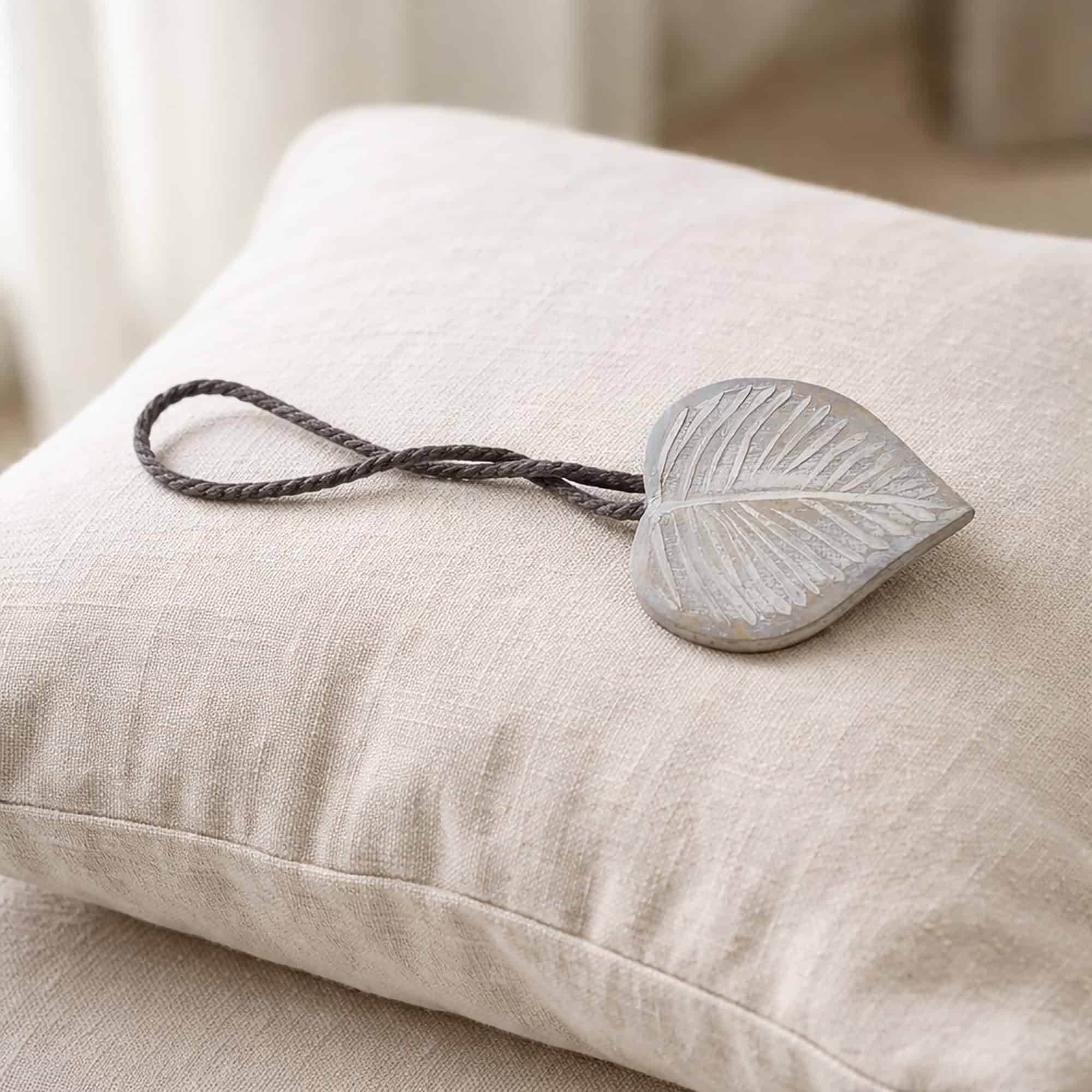 Gray wooden leaf tieback with gray cord on linen cushion