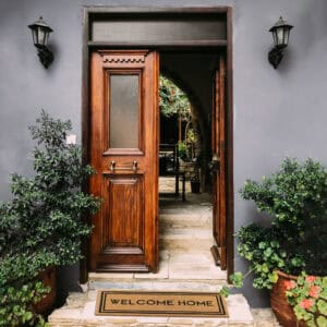 Elegant Entrance with Welcome Home Doormat: A stylish wooden front door complemented by a "Welcome Home" coir doormat and potted plants.