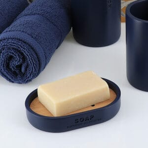 Navy blue soap dish with bamboo slotted insert holding a standard bar of soap, displayed alongside neatly rolled navy towels.
