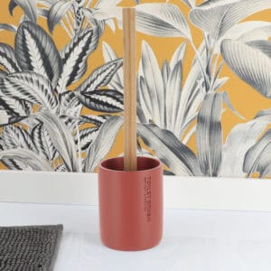 Terracotta toilet brush and holder displayed on bathroom floor with botanical wallpaper backdrop
