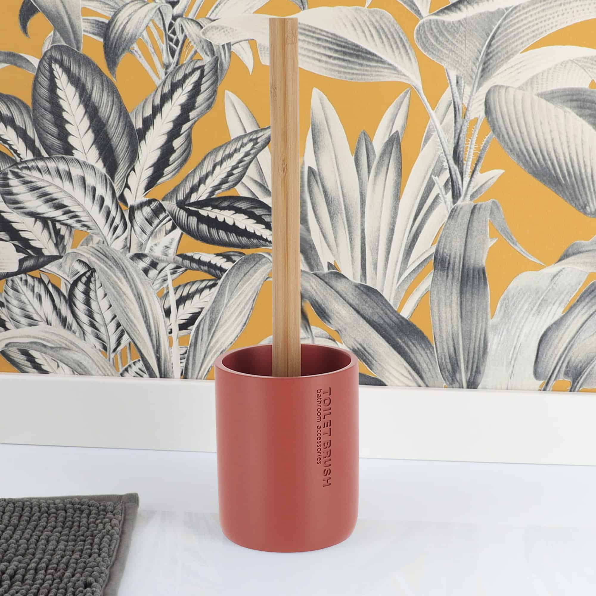 Terracotta toilet brush with bamboo handle, elegantly styled against a vibrant botanical wallpaper and a gray rug for a contemporary look.