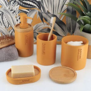 Mustard yellow bathroom accessories styled together with bamboo accents, including a lotion dispenser, tumbler, soap dish, and cotton jar.