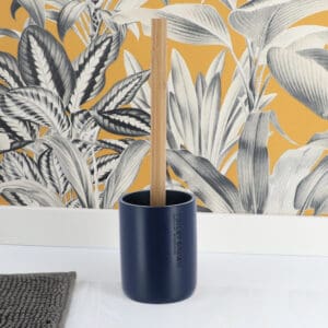 A navy blue toilet brush with a bamboo handle placed in its holder, displayed in a minimalistic setting with a yellow patterned background.