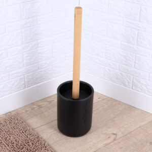 Black toilet brush holder with a bamboo handle on a wooden bathroom floor.