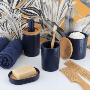 Complete bathroom accessory set in navy blue with bamboo accents, including soap dish, lotion dispenser, tumbler, and cotton jar, styled on a modern countertop.