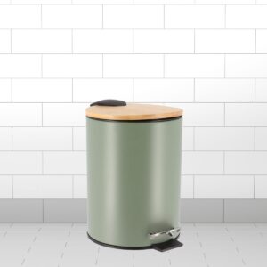 Green trash bin with bamboo lid and pedal mechanism placed on a tiled bathroom floor.