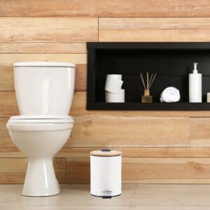 A minimalist bathroom with wooden paneling featuring a white step trash can with a bamboo lid, adding a touch of style and functionality.