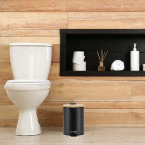 A minimalist bathroom with wooden paneling featuring a black step trash can with a bamboo lid, adding a touch of style and functionality.
