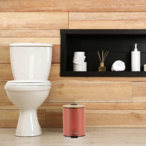 A minimalist bathroom with wooden paneling featuring a red step trash can with a bamboo lid, adding a touch of style and functionality.