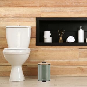 A minimalist bathroom with wooden paneling featuring a green step trash can with a bamboo lid, adding a touch of style and functionality.