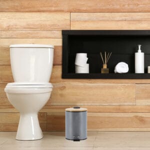 A minimalist bathroom with wooden paneling featuring a gray step trash can with a bamboo lid, adding a touch of style and functionality.