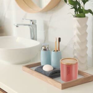 Terracotta cotton jar with bamboo lid styled on a bathroom tray, surrounded by matching accessories and a minimalist sink setup.