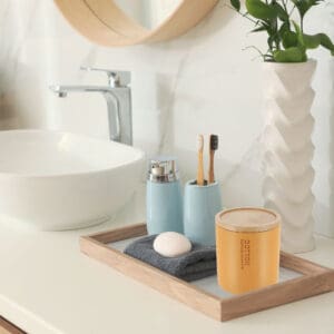 Mustard yellow cotton jar with bamboo lid styled on a bathroom tray, surrounded by matching accessories and a minimalist sink setup.