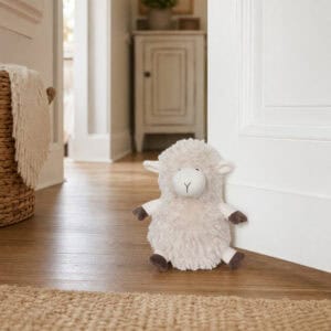 Cream sheep door stopper propping open a white paneled door on hardwood floor, woven basket and cabinet in the background.