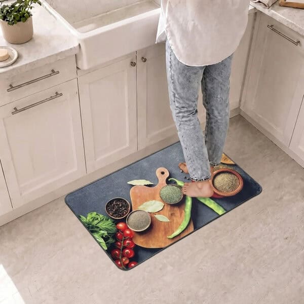 A person stands in slippers on the kitchen mat in front of a white farmhouse sink, the spice and herb photo brightening the floor.