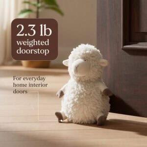 Cream sheep door stopper propping open a dark wood door on hardwood floor. On-image text: "2.3 lb weighted doorstop," "For everyday home interior doors."