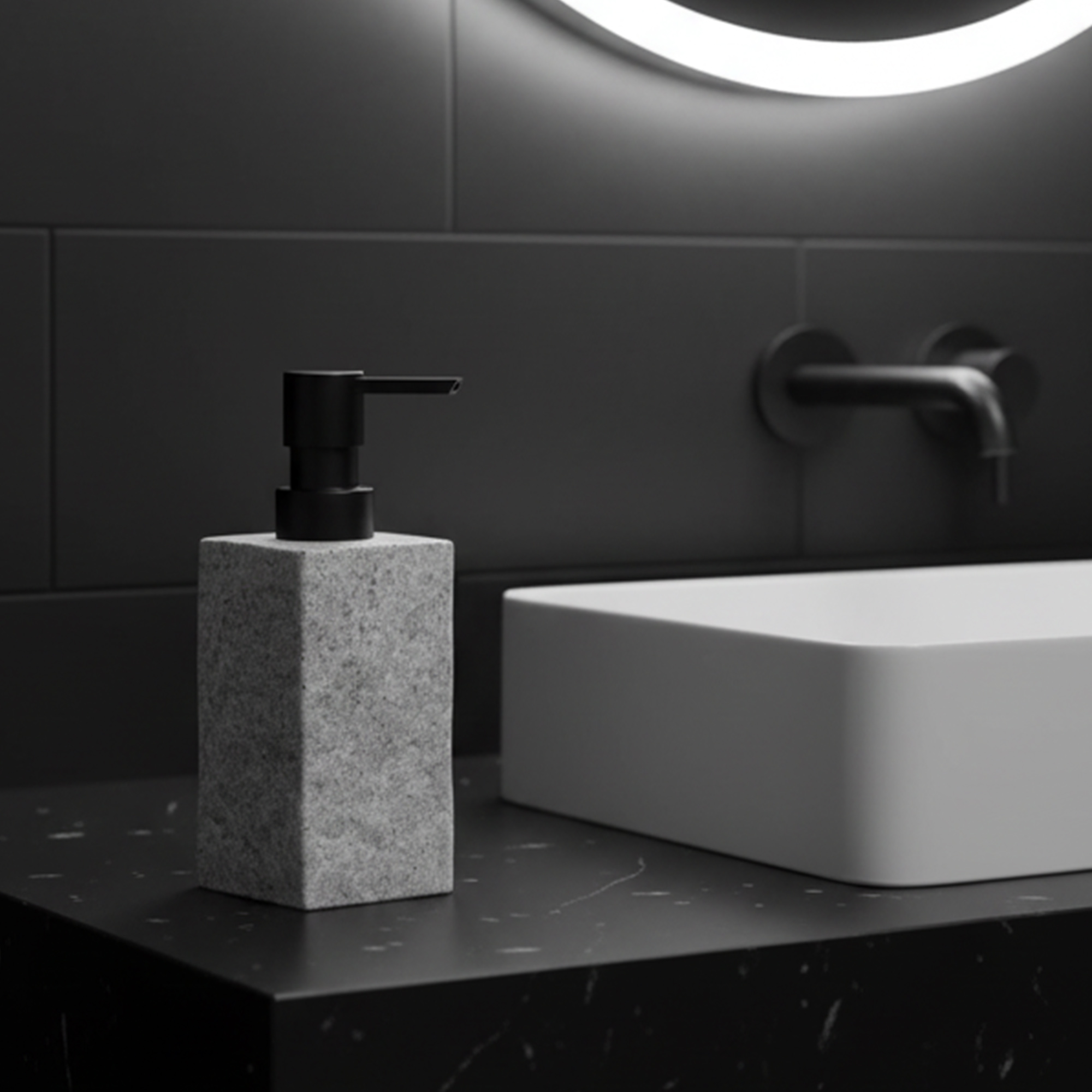 Gray stone effect soap dispenser with black pump beside sink under round mirror