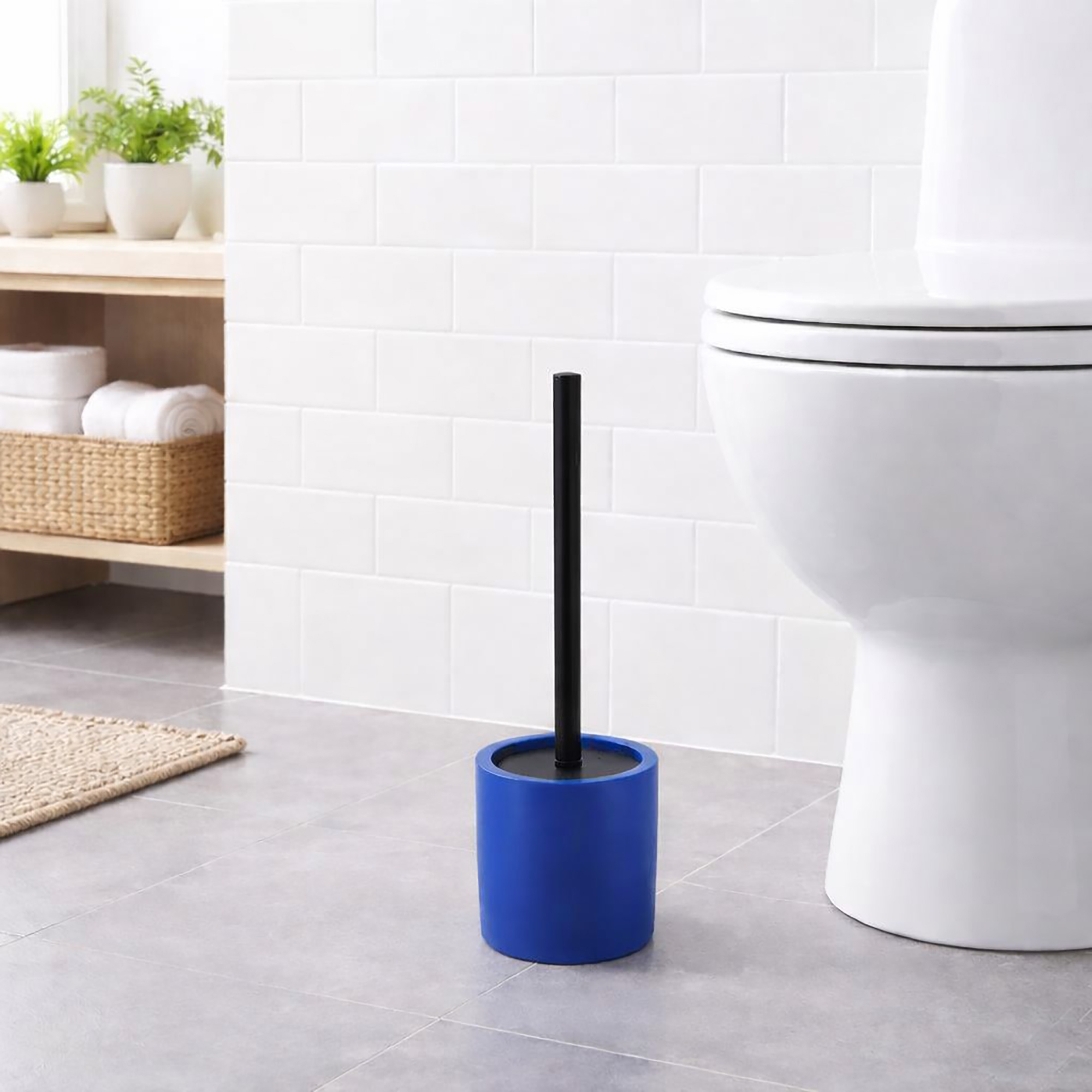 Modern blue toilet brush with black handle in cylindrical holder, positioned on bathroom floor beside white toilet