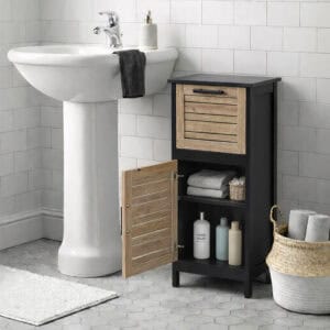 "Open louvered cabinet door revealing two shelves with towels and toiletries, beside a pedestal sink"