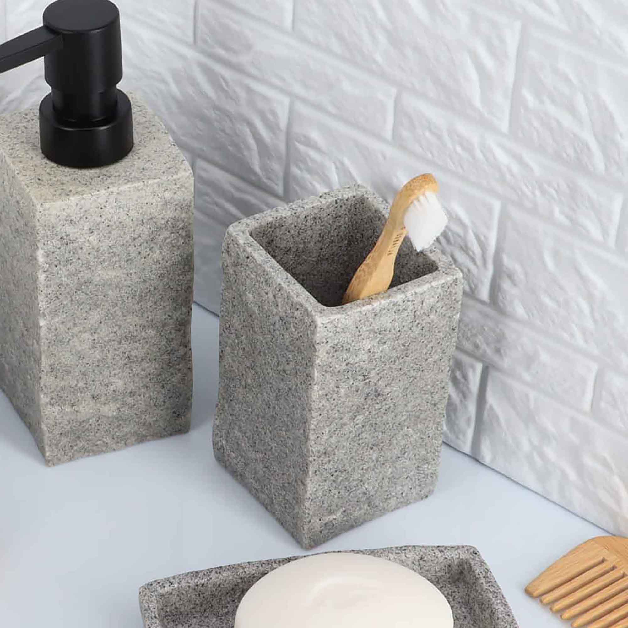 A gray stone-effect bathroom tumbler holding a toothbrush, displayed alongside a matching soap dispenser on a countertop.