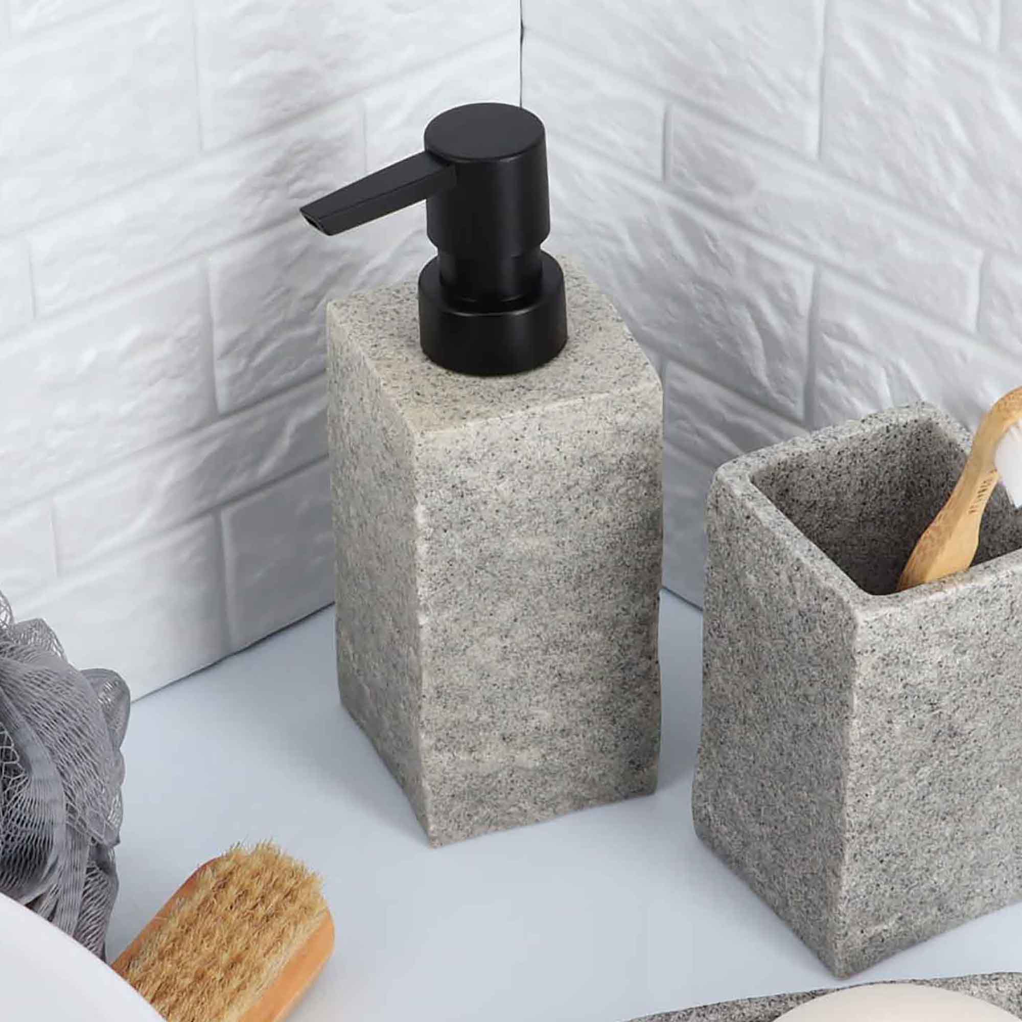 A gray stone-effect soap dispenser with a black pump, displayed next to a matching toothbrush holder on a bathroom countertop.