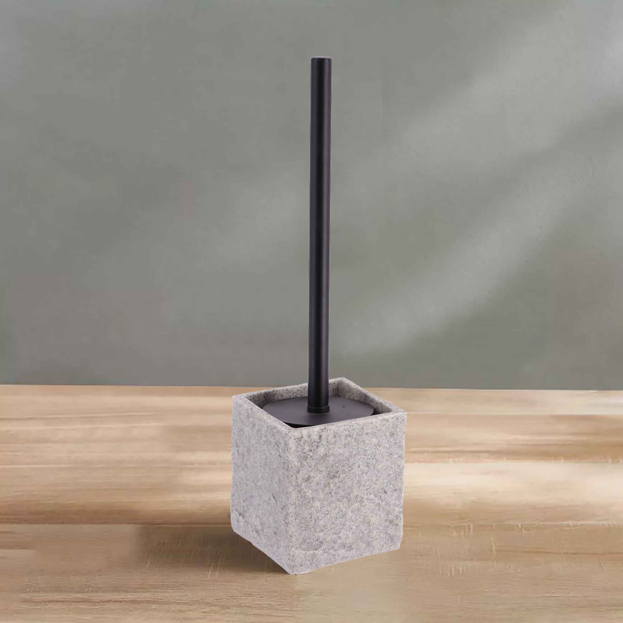 A gray stone-effect toilet brush holder with a black handle, displayed on a wooden surface against a soft green wall for a clean aesthetic.