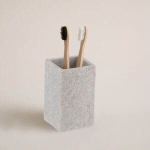 A gray stone-effect bathroom tumbler holding two bamboo toothbrushes, displayed against a neutral background for a clean and natural look.