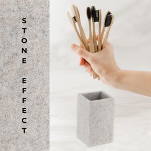 A close-up of a gray stone-effect bathroom tumbler next to a hand holding multiple bamboo toothbrushes, emphasizing its modern design and practicality.