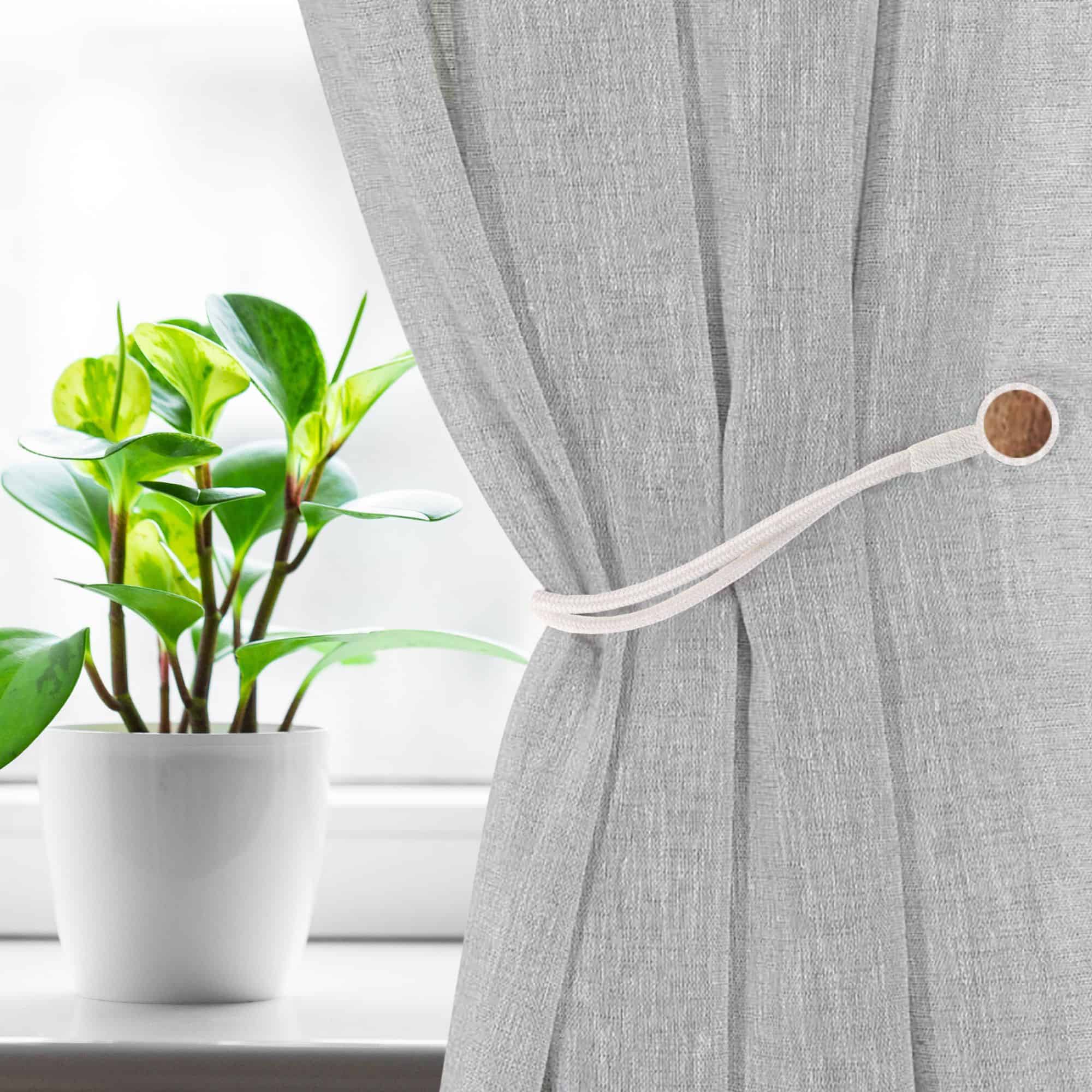 Magnetic Curtain Tieback Holding Gray Curtain – A white magnetic tieback securing a gray curtain near a window.