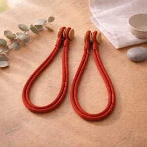 Rust red braided rope curtain tiebacks with a wooden magnetic closure, displayed on a wooden surface.