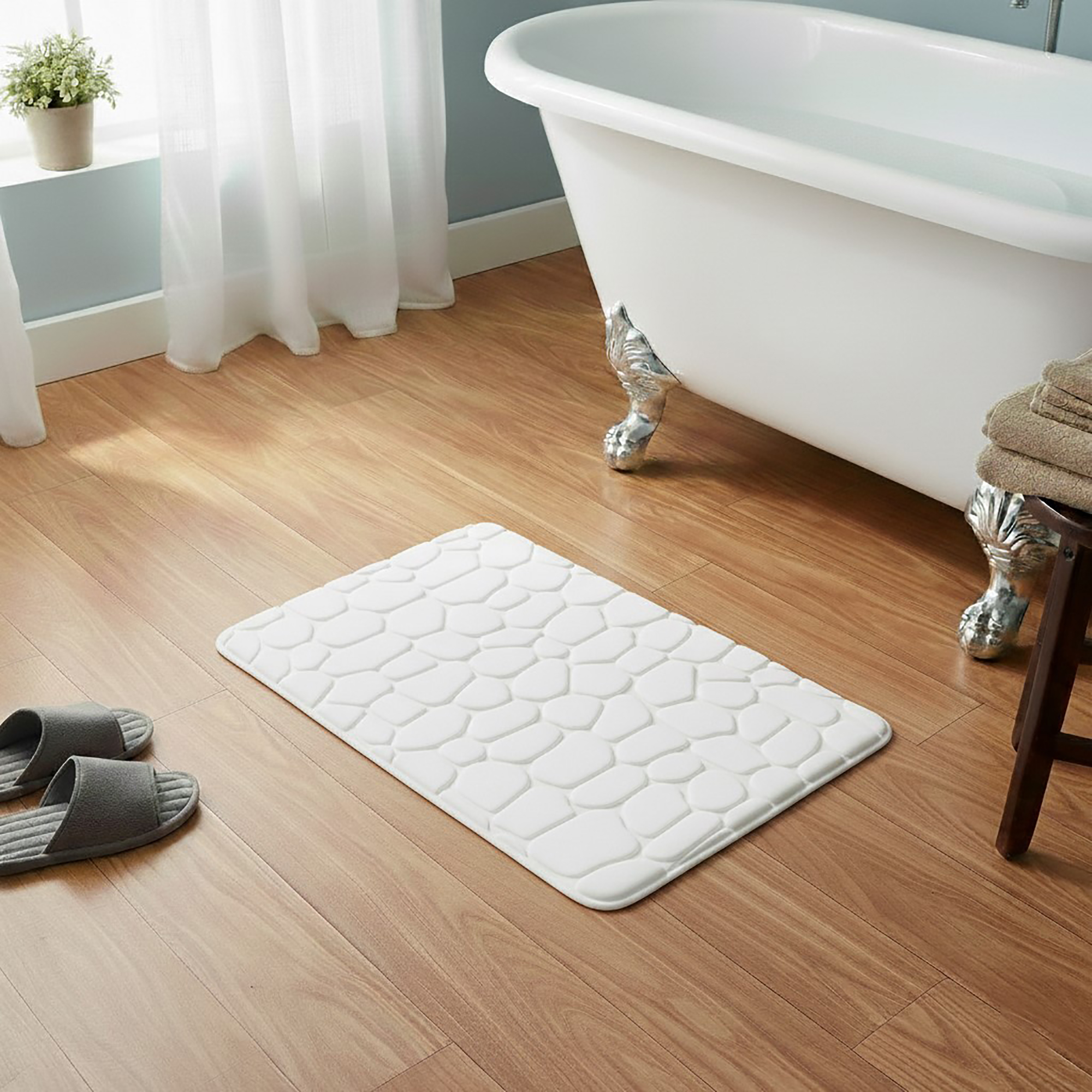 White memory foam bath mat with embossed pebble stone texture on wooden floor beside clawfoot tub
