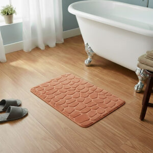 Copper memory foam bath mat with embossed pebble stone texture on wooden floor beside clawfoot tub