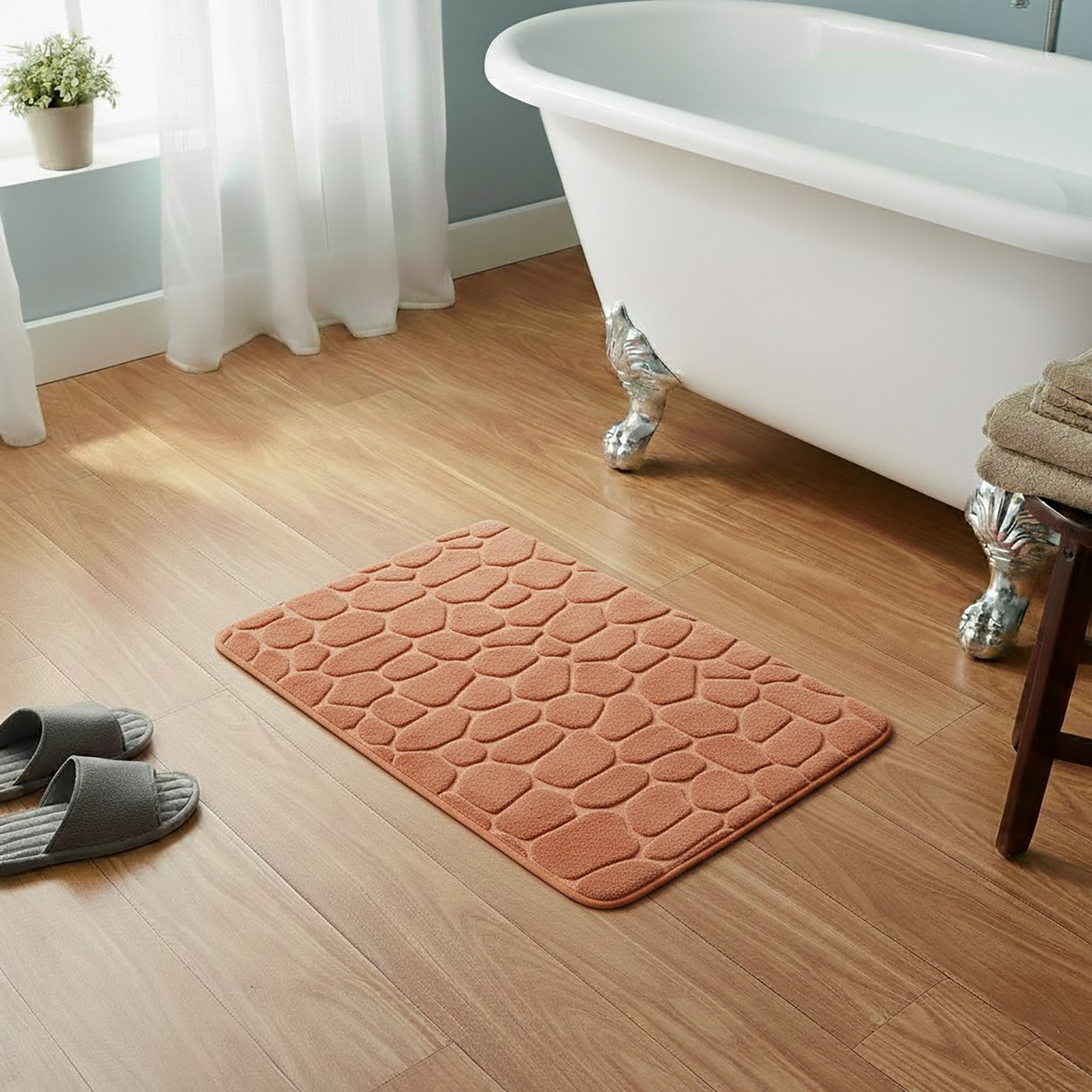 Copper memory foam bath mat with embossed pebble stone texture on wooden floor beside clawfoot tub