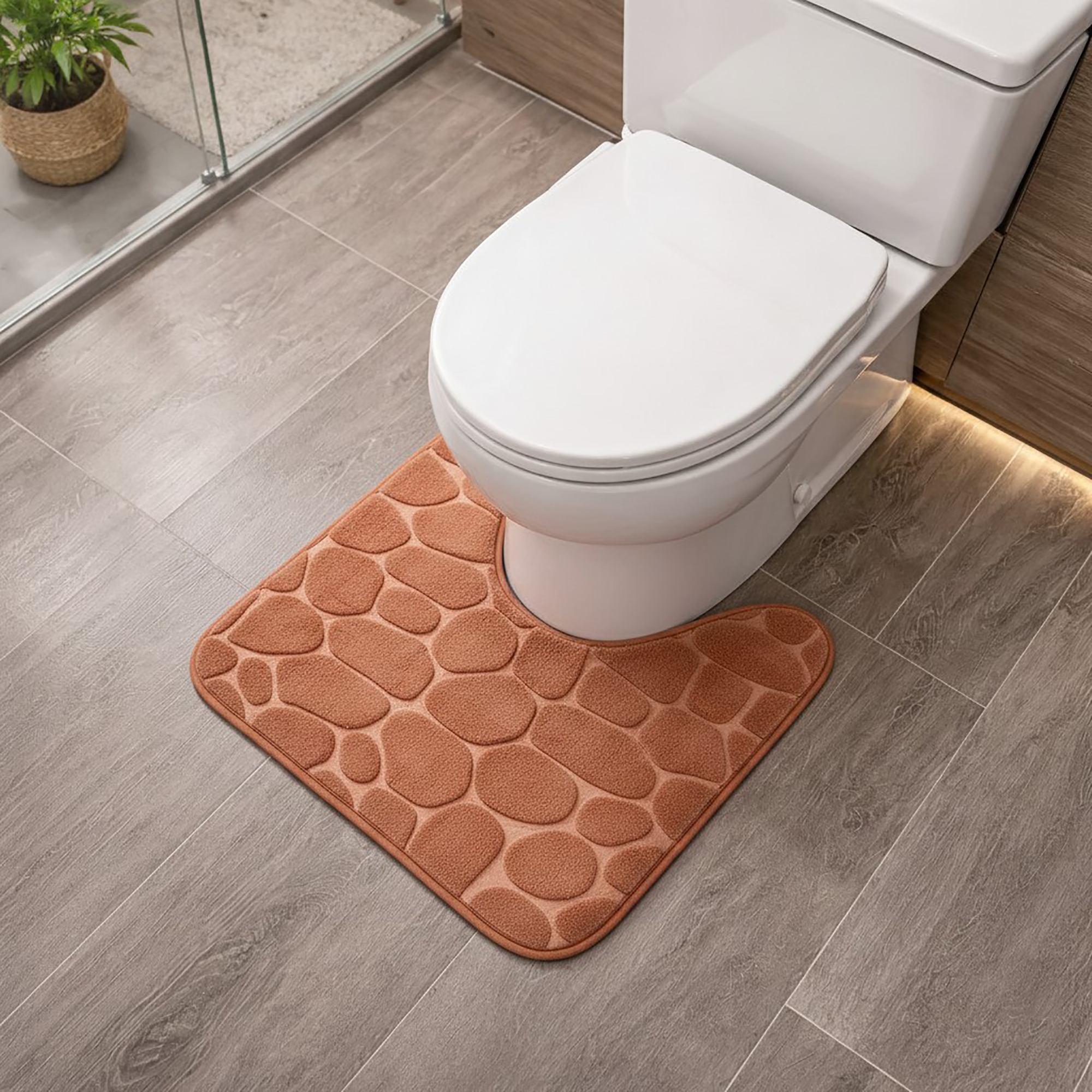 Copper memory foam contour bath mat with pebble texture positioned around toilet base, angled view