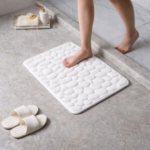 Barefoot stepping on a soft white pebble design memory foam mat placed on a bathroom tile floor
